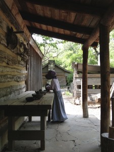 Grinding corn, wheat and coffee by hand outside the Seela Cabin, Log Cabin Village