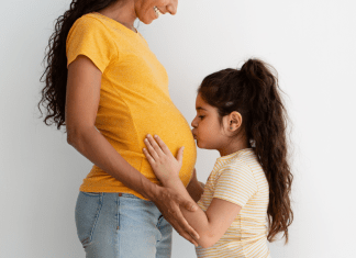 Big sister kisses her mom's pregnant belly.