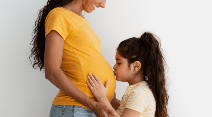 Big sister kisses her mom's pregnant belly.