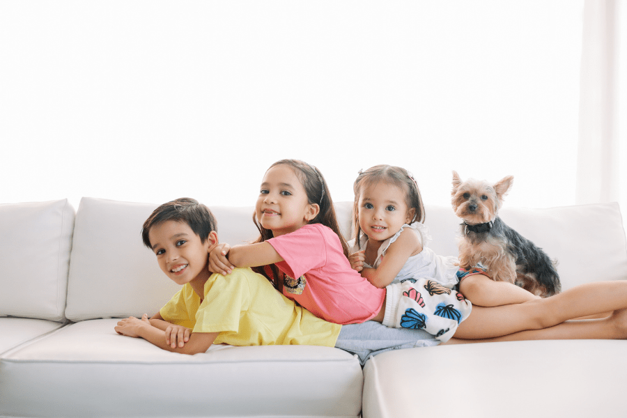 3 siblings and a dog pose together on a couch