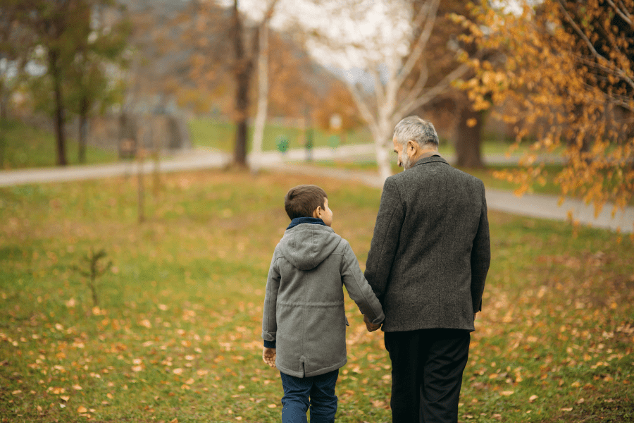 Grandpa and grandson go on a walk through a park hand in hand.