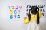 Little girl in pig tails points to letters on a chart.