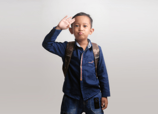 Kindergarten boy waves a salute goodbye as he wears a backpack and heads to school.