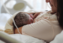 New mom looks lovingly at breastfeeding newborn while laying in hospital bed.