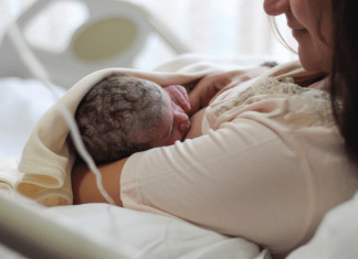 New mom looks lovingly at breastfeeding newborn while laying in hospital bed.