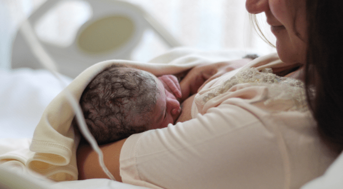 New mom looks lovingly at breastfeeding newborn while laying in hospital bed.