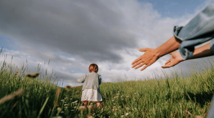 Toddler girl runs away from her mother in a meadow.