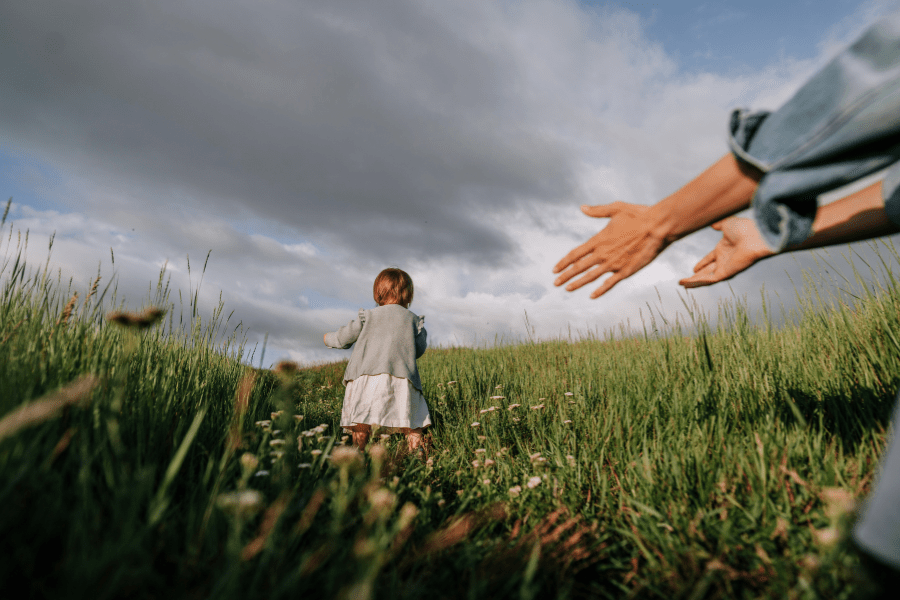 Toddler girl runs away from her mother in a meadow.