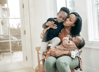 Tired mama holds a baby on her lap and her toddler in her arms as she kisses and loves on them.