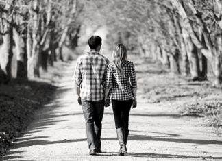 A black and white picture of a couple walking silently through a grove of trees.