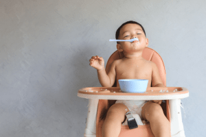 Toddler boy plays with his spoon while sitting in a high chair.