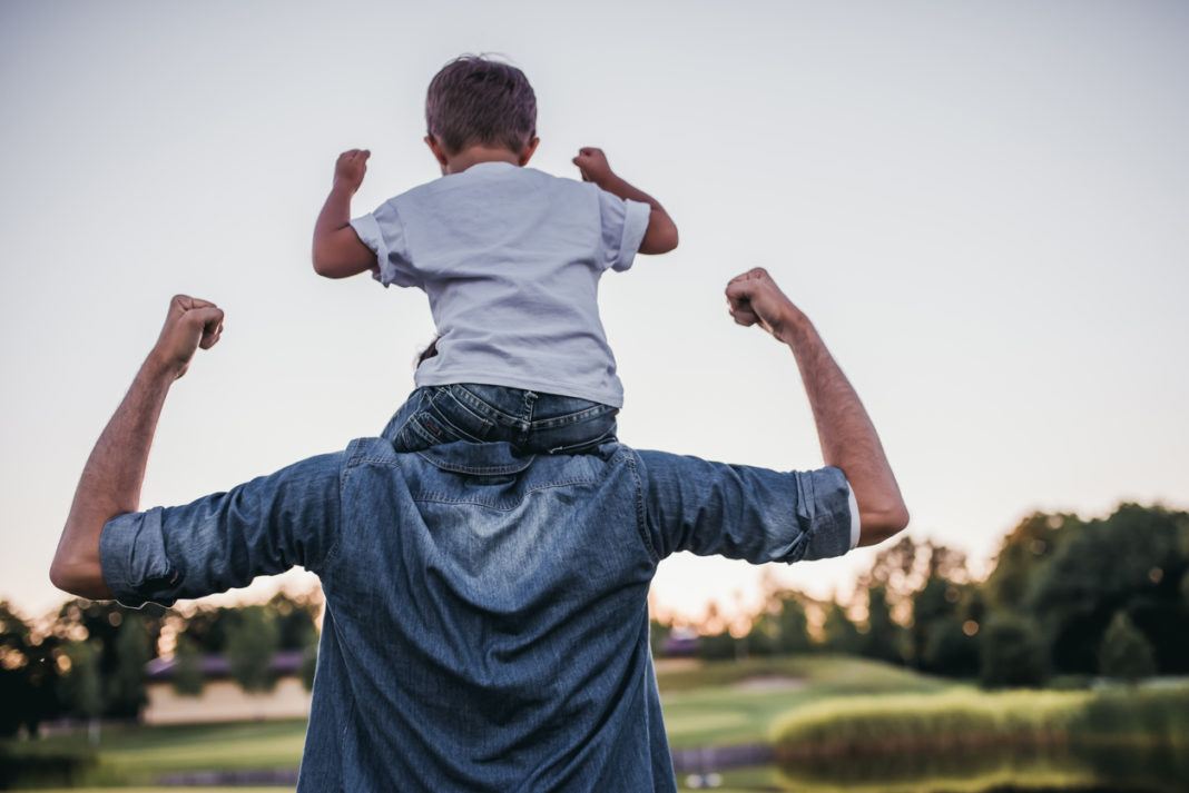 Young boy is sitting on his father's shoulders.