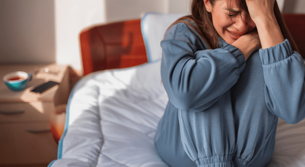 Woman cries sitting on her bed.