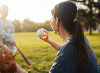 A mom throws a baseball to her son at bat.