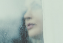 Woman looks through a rainy, foggy window.