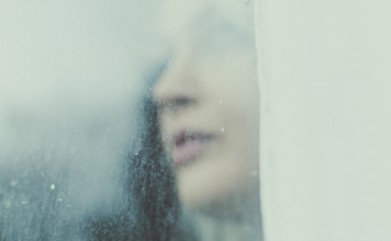 Woman looks through a rainy, foggy window.