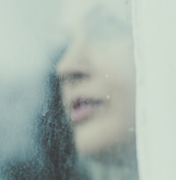 Woman looks through a rainy, foggy window.