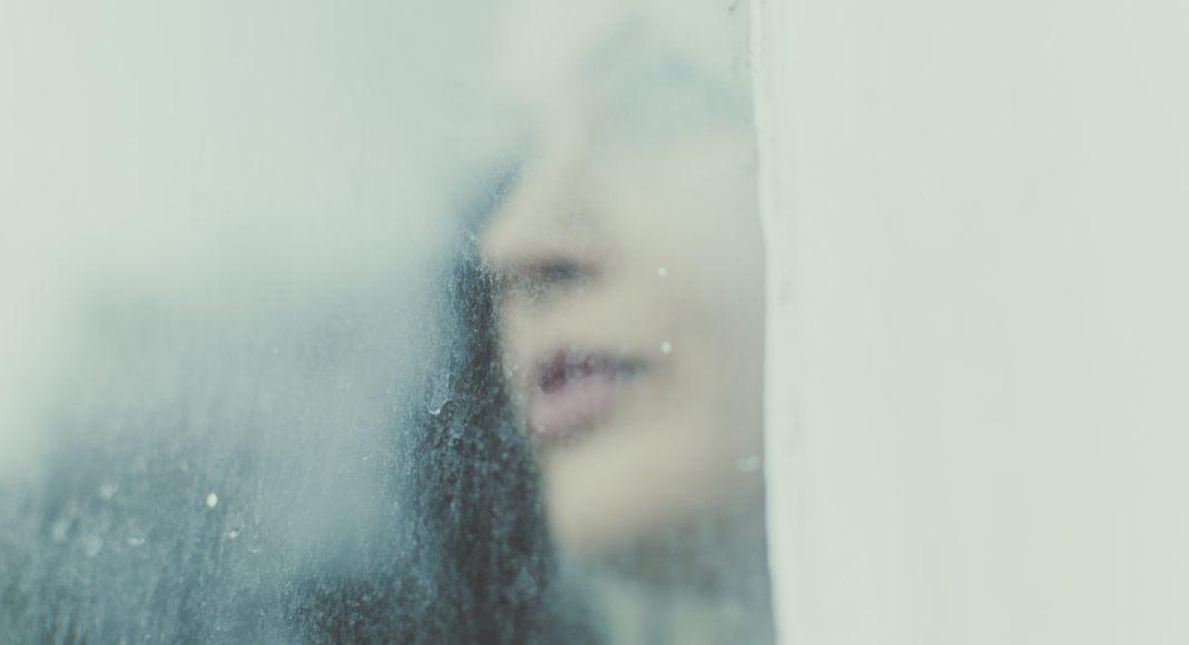 Woman looks through a rainy, foggy window.