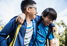 Brothers laugh with their arms over each other's shoulders walking to school.