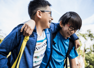 Brothers laugh with their arms over each other's shoulders walking to school.