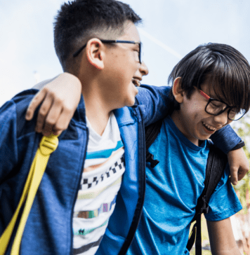 Brothers laugh with their arms over each other's shoulders walking to school.