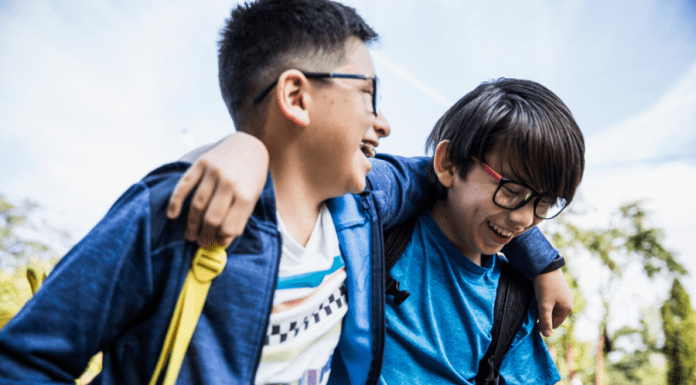 Brothers laugh with their arms over each other's shoulders walking to school.