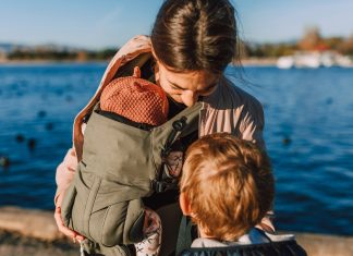 mother wearing a baby while talking to young child, pros of babywearing