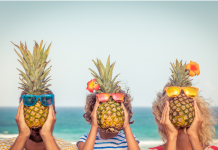 Mom, dad, and child hold pineapples wearing sunglasses in front of their faces.