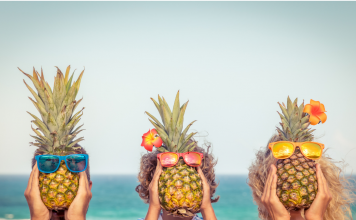 Mom, dad, and child hold pineapples wearing sunglasses in front of their faces.