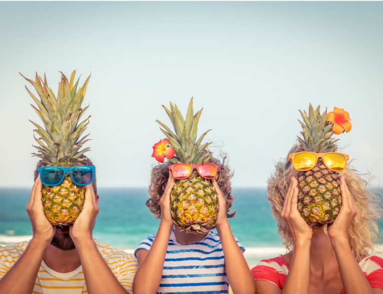 Mom, dad, and child hold pineapples wearing sunglasses in front of their faces.