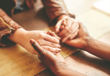 Women hold hands across a desk.