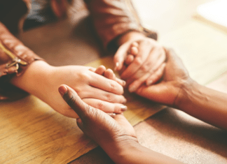 Women hold hands across a desk.