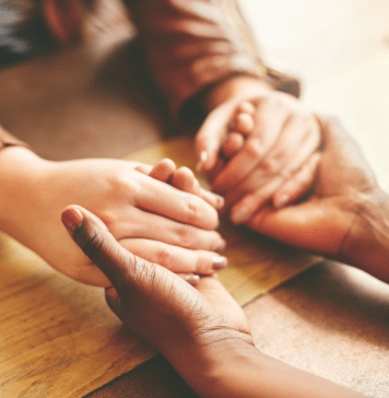 Women hold hands across a desk.