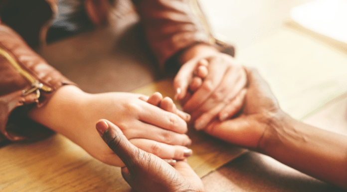 Women hold hands across a desk.