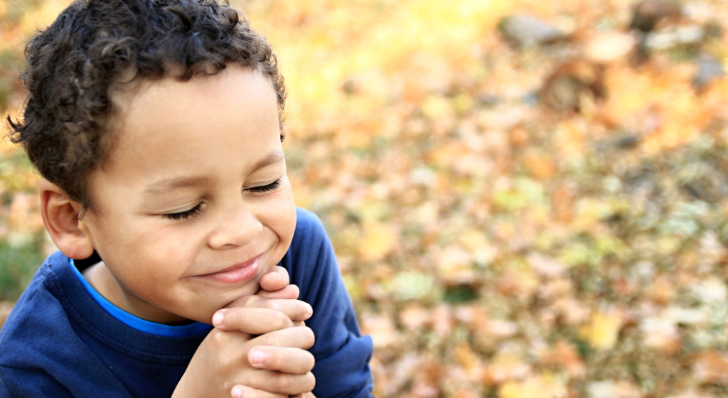 A young boy grasps his hands and closes his eyes.