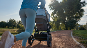 A mom pushes a baby stroller on her run outside on a running path.