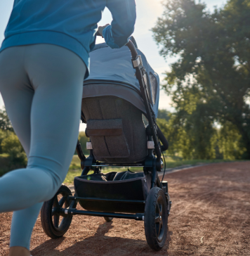 A mom pushes a baby stroller on her run outside on a running path.