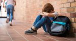 A young male student sits against the brick wall and expresses frustration.