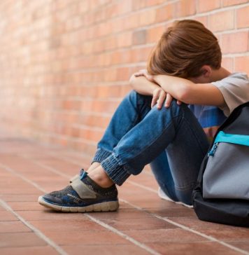 A young male student sits against the brick wall and expresses frustration.