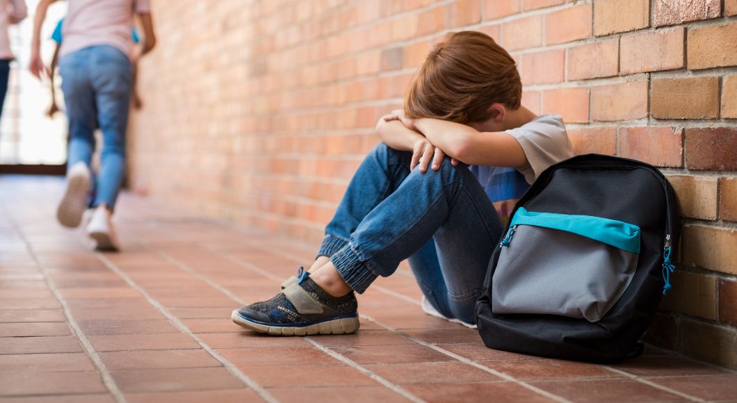 A young male student who hates school sits against the brick wall and expresses frustration.