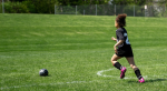 Young girl running toward a soccer ball on an open soccer field