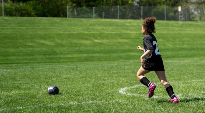 Young girl running toward a soccer ball on an open soccer field