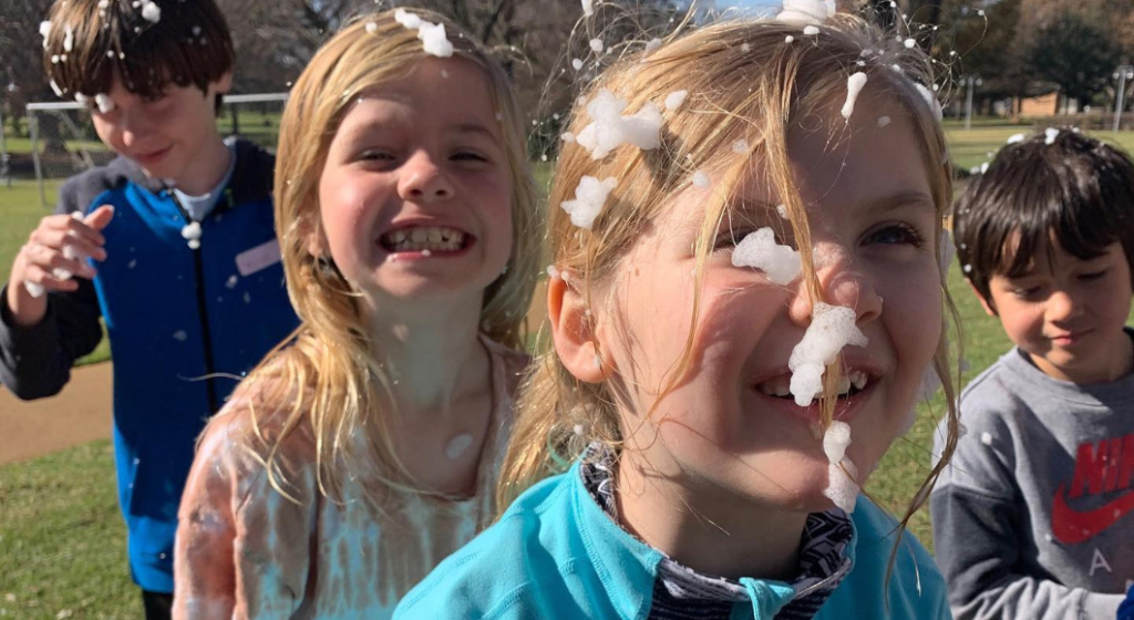 close-up of smiling young children playing in foam spray in a field