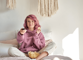 A woman lays in bed with chips while watching tv.