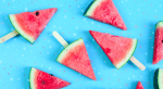 frozen slices of watermelon with Popsicle sticks in them, laying on a bright blue background with splotches of color throughout