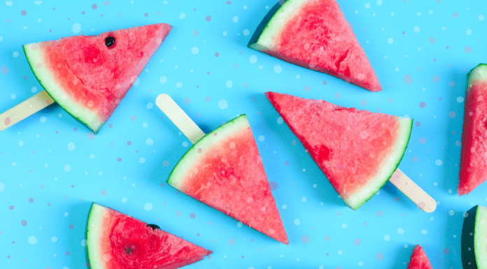 frozen slices of watermelon with Popsicle sticks in them, laying on a bright blue background with splotches of color throughout