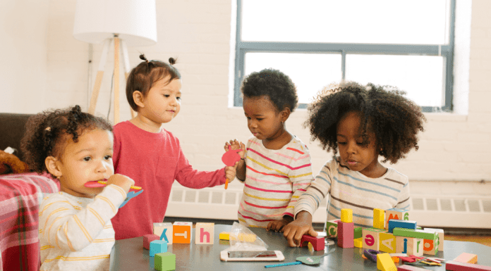 Toddlers stand around a table.