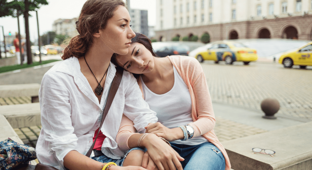 A woman leans her head on her friend's shoulder.