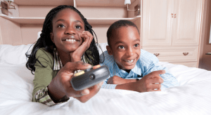 Two kids watch tv while the girl holds a remote.