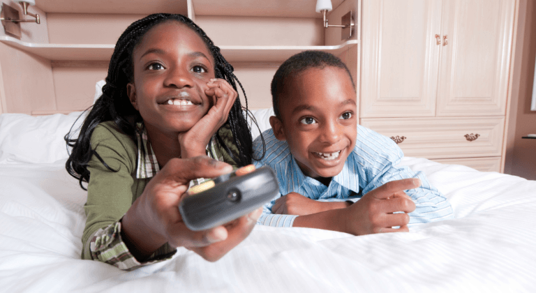 Two kids watch tv while the girl holds a remote.